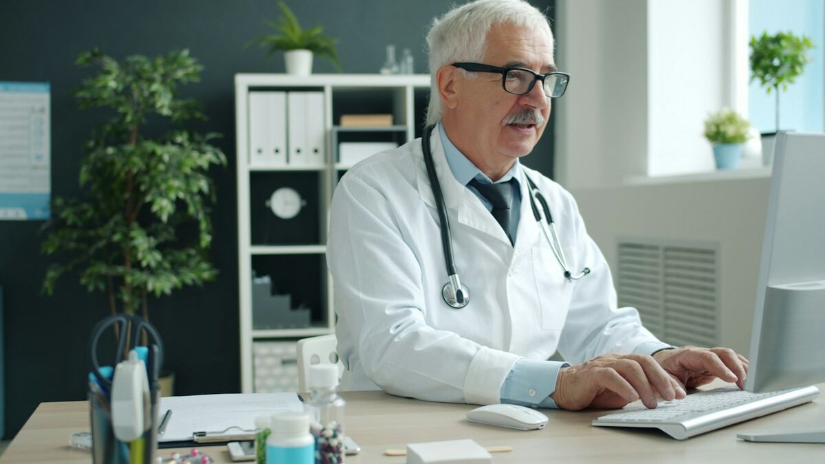 A physician working at a desk with a laptop in a bright office.